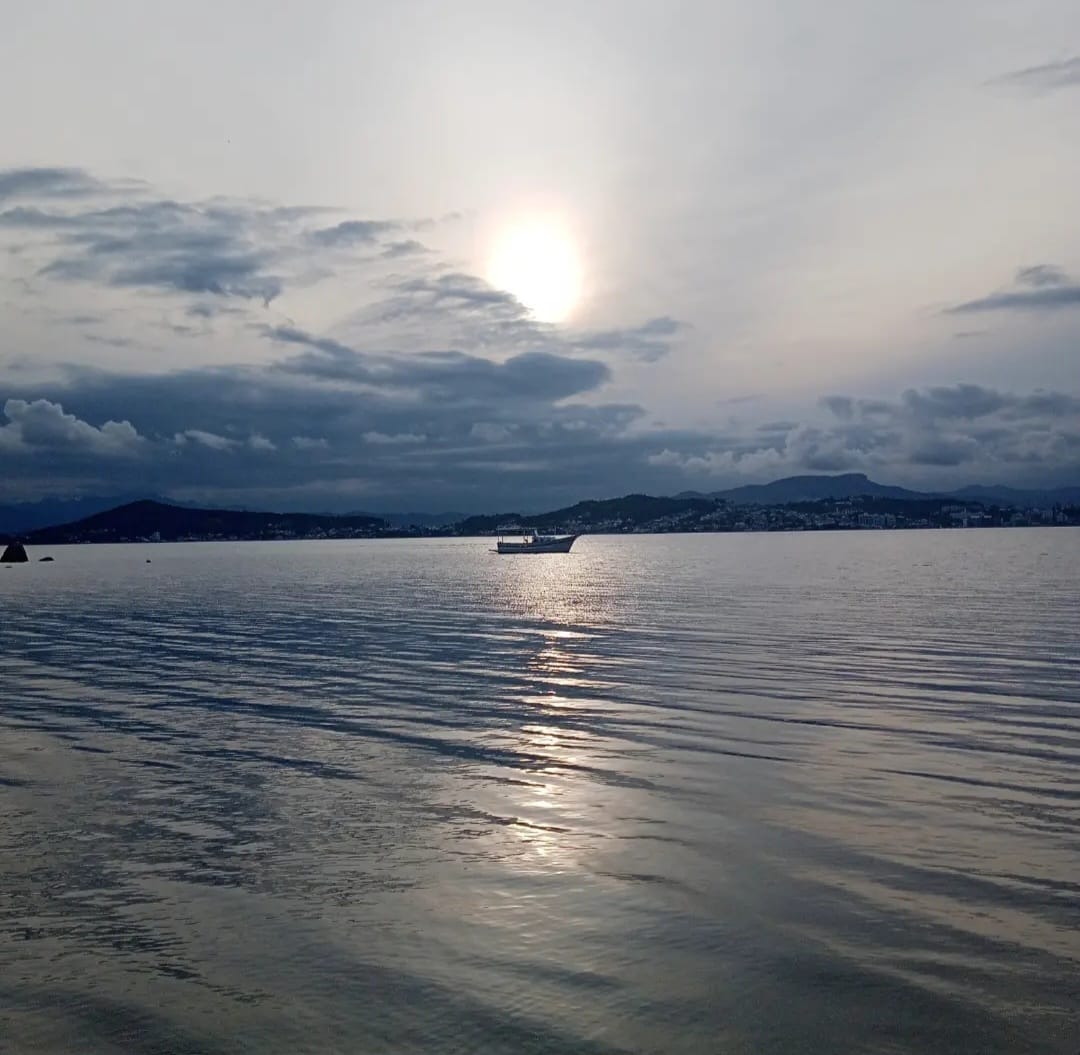 Barco solitário em mar prateado sob céu encoberto